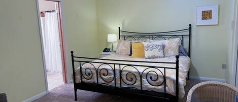 Un dormitorio con cama, mesita de noche, lámpara y una silla de mimbre.
