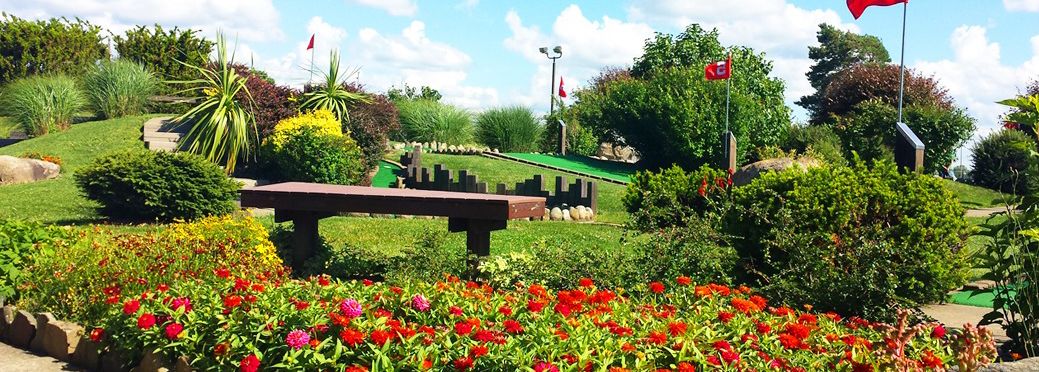 Um parque com um banco, canteiros de flores e um campo de golfe.
