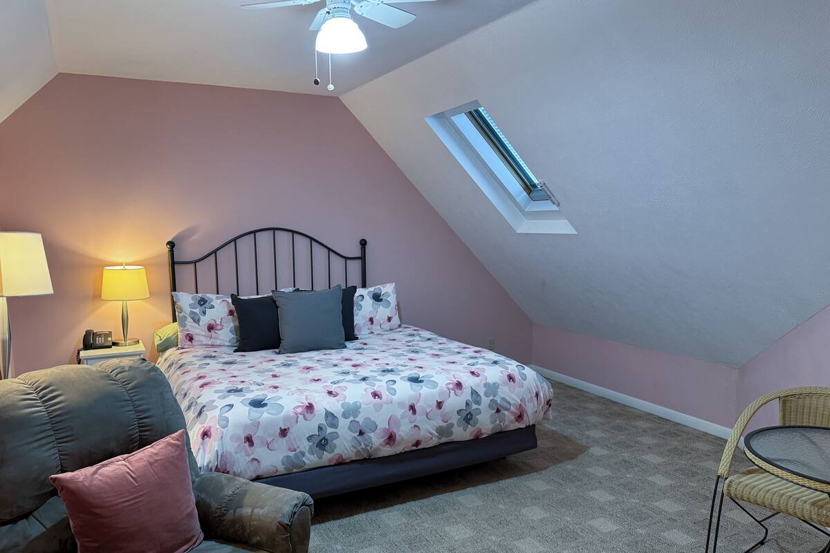 Une chambre à coucher avec un lit, une table de chevet, une lampe, une chaise et une lucarne.