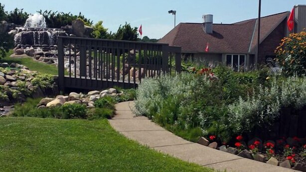 Un jardin aménagé avec un sentier, une cascade et un bâtiment sur lequel flotte un drapeau rouge.
