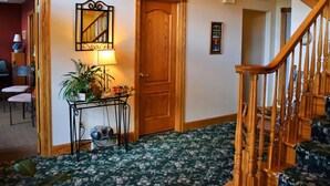 Un couloir avec une porte en bois, une petite table avec une lampe et un escalier.
