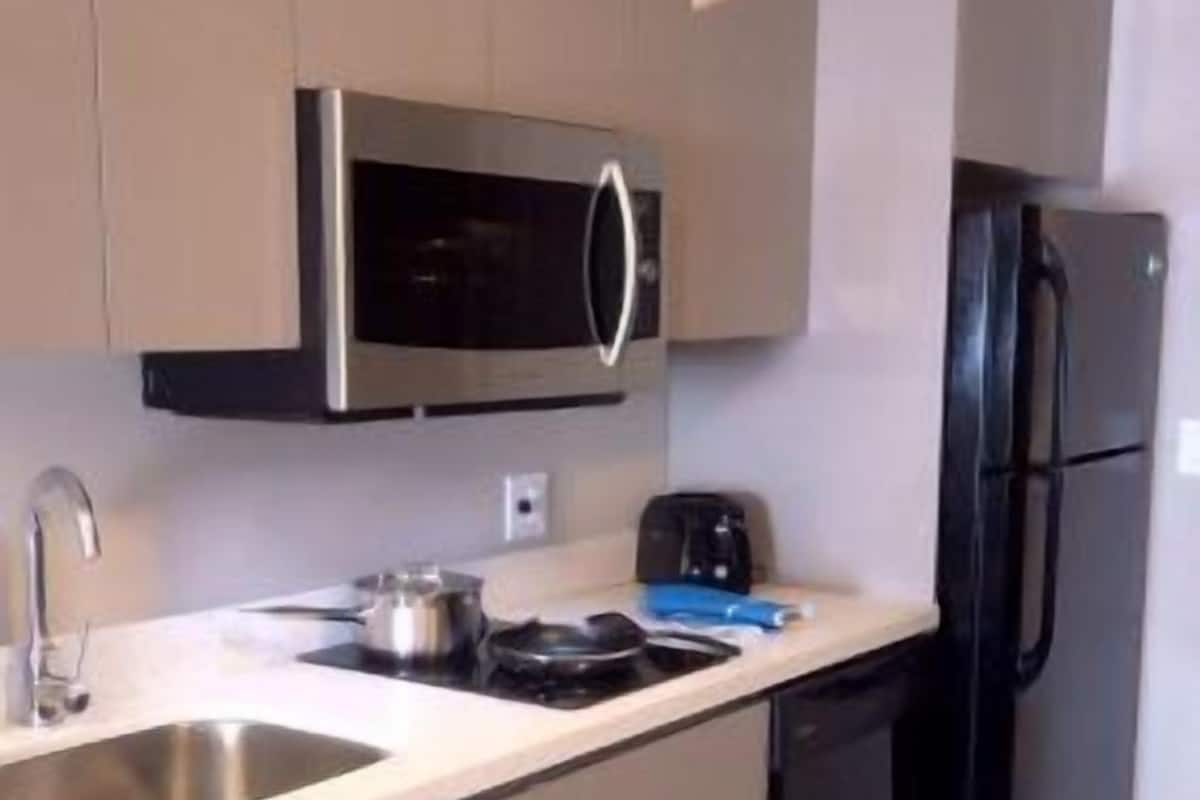 Une cuisine compacte équipée d’un four à micro-ondes, d’un grille-pain, d’un évier et d’un réfrigérateur noir.