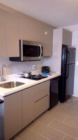 Cocina compacta con microondas, tostadora, lavabo y refrigerador negro.