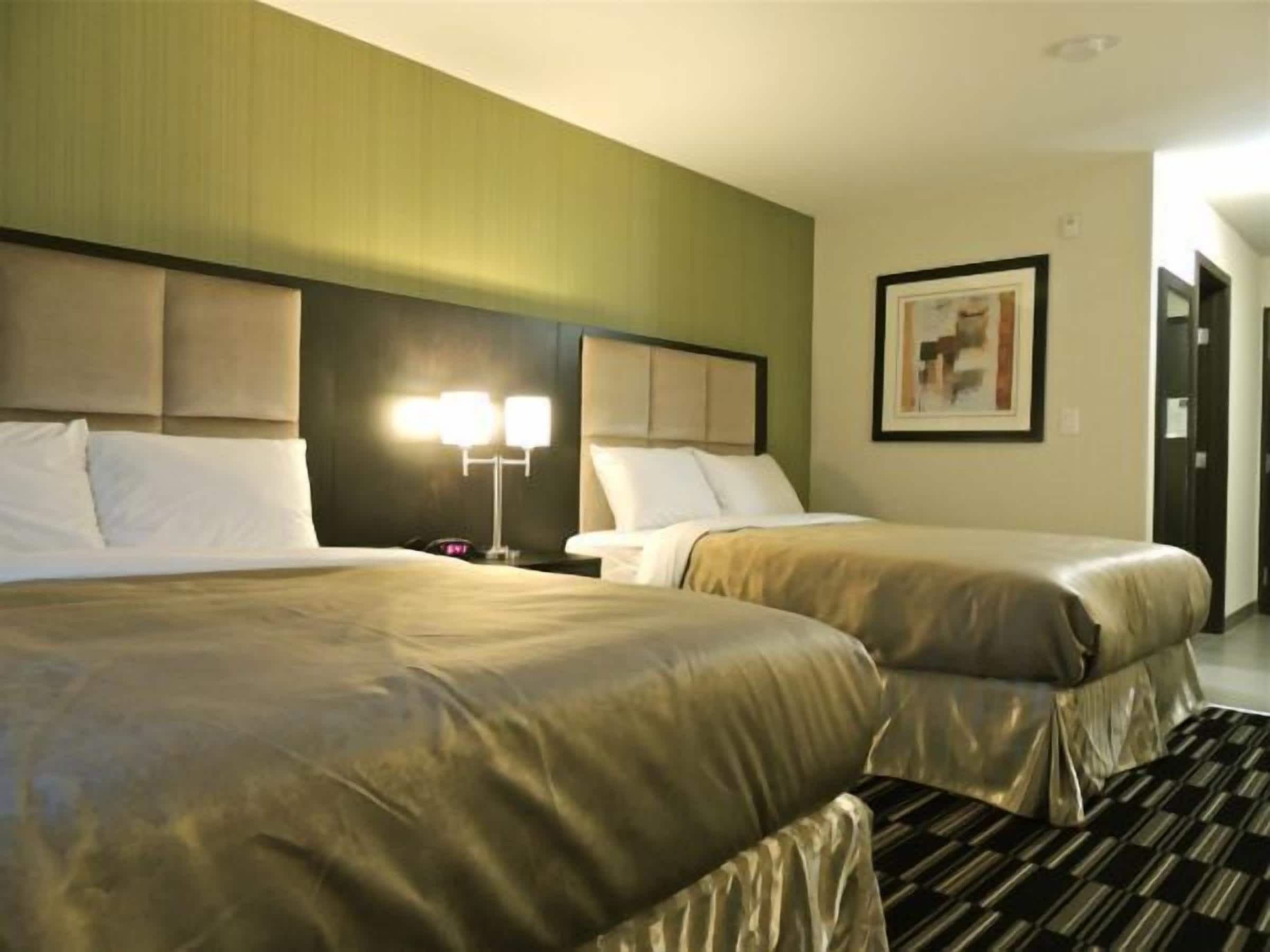 Ein Hotelzimmer mit zwei Betten, einem Nachttisch mit Lampe und einem gerahmten Bild an der Wand.