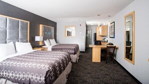 Una habitación de hotel con dos camas, un escritorio, una silla, un espejo y una pequeña cocina.