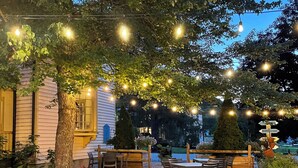 An outdoor patio area with string lights, wooden tables and chairs, and a stone pathway.