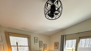 A bedroom with a large bed, a bedside table with a lamp, a window with blinds, and a view of the outdoors.