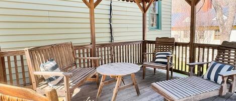 Eine Holzterrasse mit überdachtem Sitzbereich, inklusive eines runden Tisches und mehreren Stühlen.