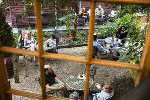 An outdoor patio with round tables and chairs, surrounded by plants and a brick wall.