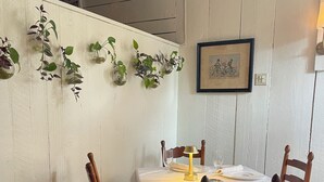 A dining area with a round table set for four, wooden chairs, a white tablecloth, and hanging plants on the wall.