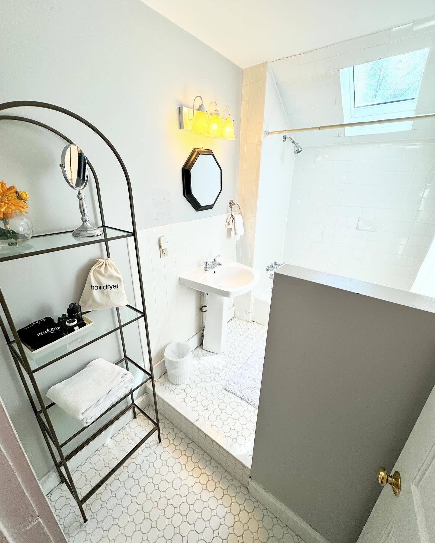 A modern bathroom with a glass shelf holding toiletries, a white sink, and a shower area.