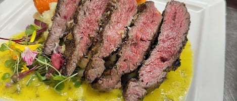 A white rectangular plate with sliced steak, vegetables, and a yellow sauce.