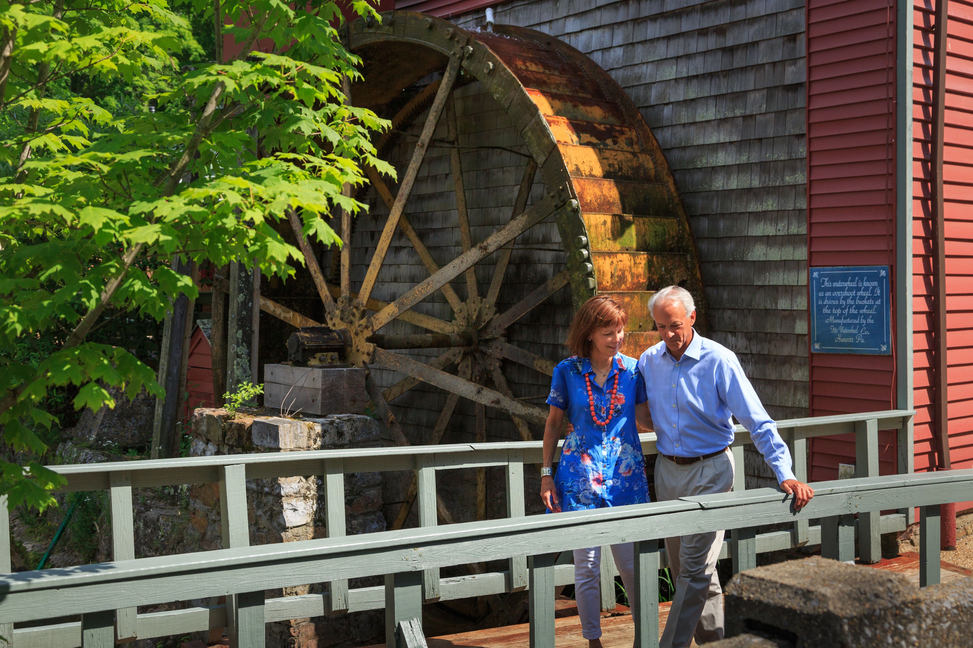 A historic water wheel and wooden building with a signboard.
