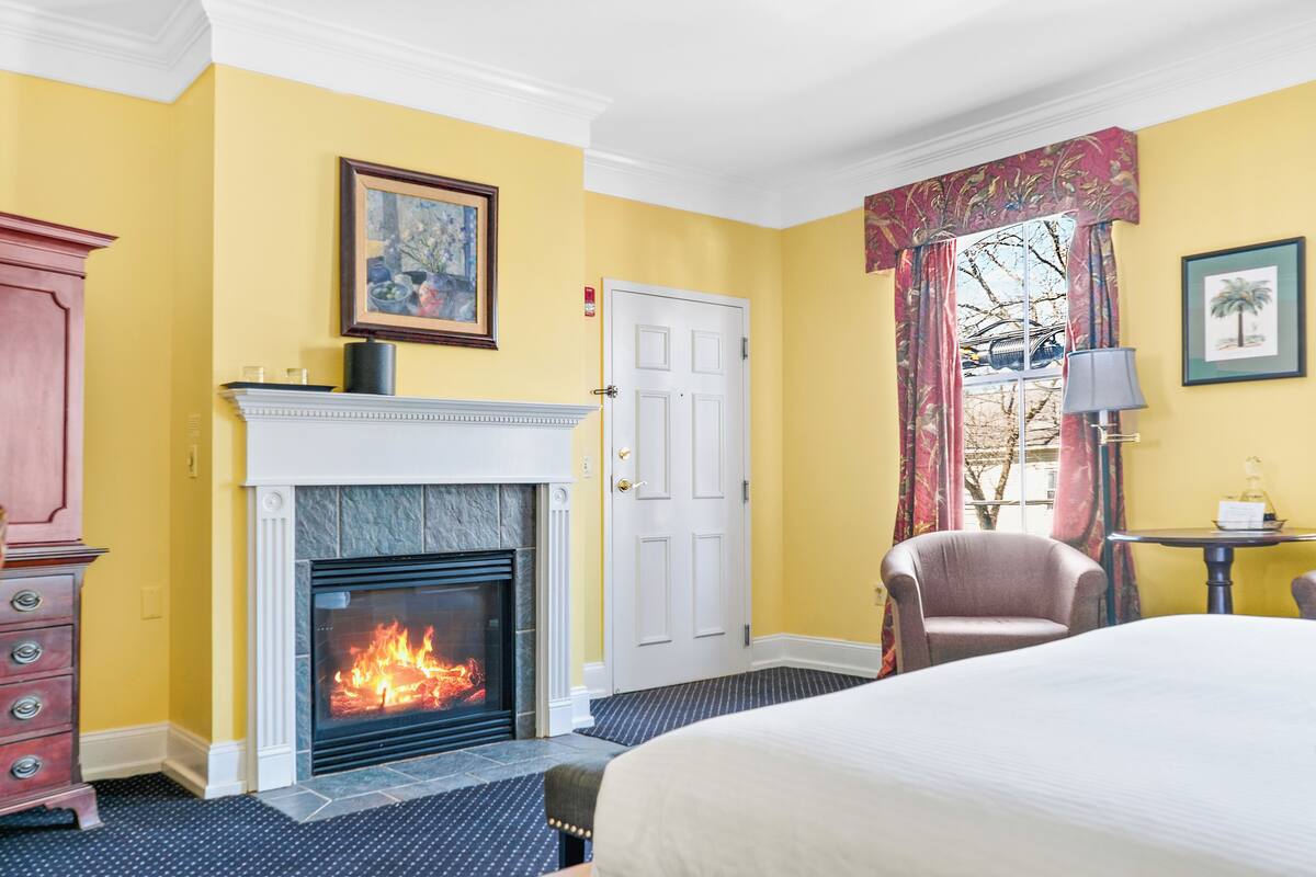 A hotel room with a fireplace, a bed, a chair, and a table.
