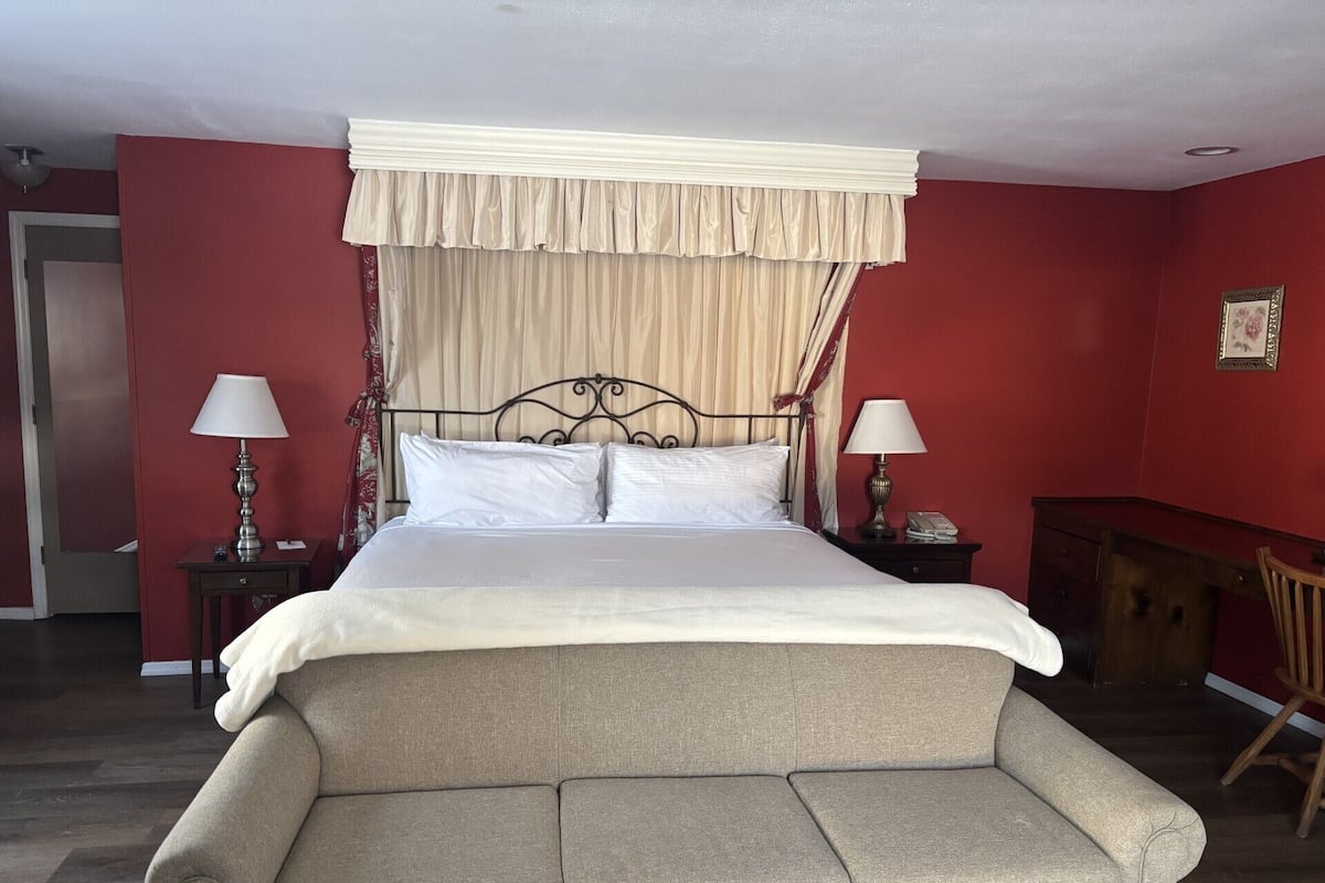A bed with a canopy, two bedside tables with lamps, a wooden chair, and a wooden bench.