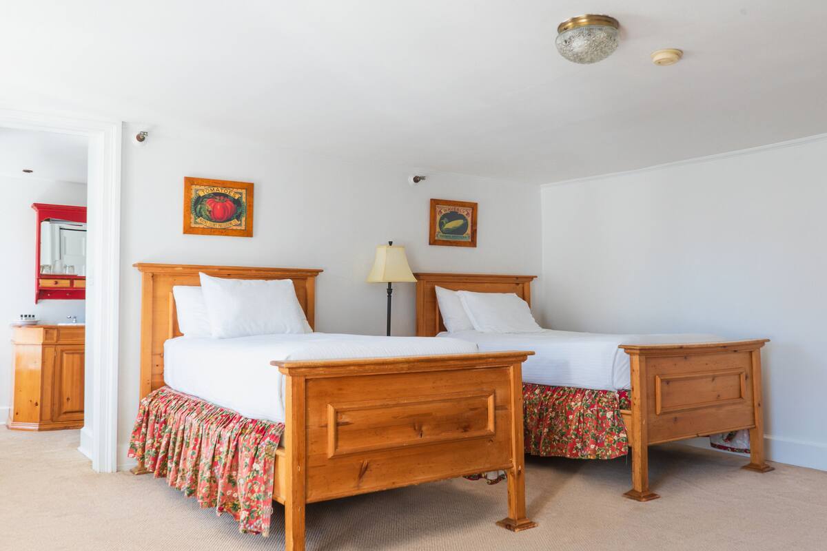 A double bed with a wooden frame and a floral skirt, a nightstand, a lamp, and two wall-mounted pictures.