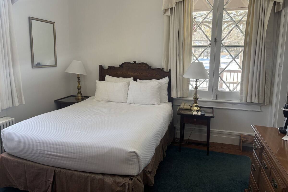 A neatly made bed with white linens, a wooden headboard, and a nightstand with a lamp.