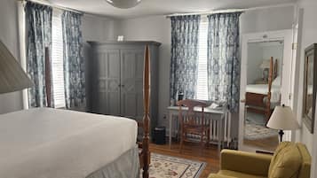 A bedroom with a four-poster bed, a desk with a chair, a yellow armchair, and a large mirror.