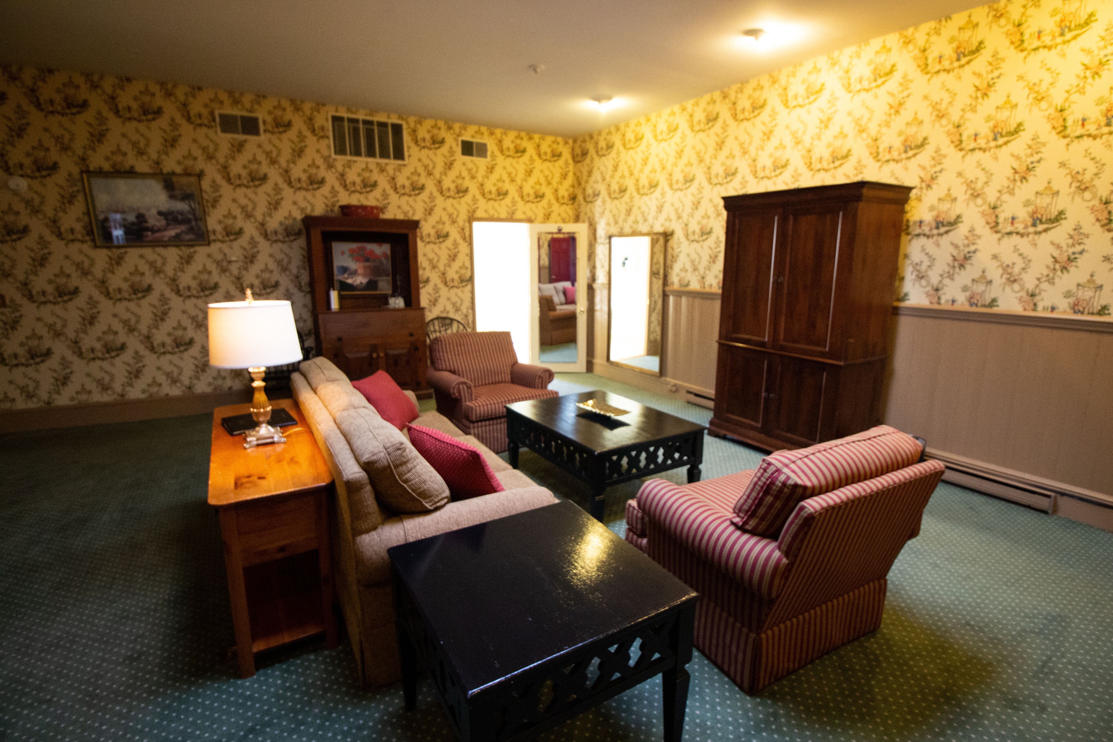 A living room with patterned wallpaper, a sofa, a striped armchair, a small table, and a cabinet.