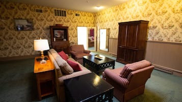 Una sala de estar con papel tapiz estampado, un sofá, un sillón a rayas, una mesita y un aparador.