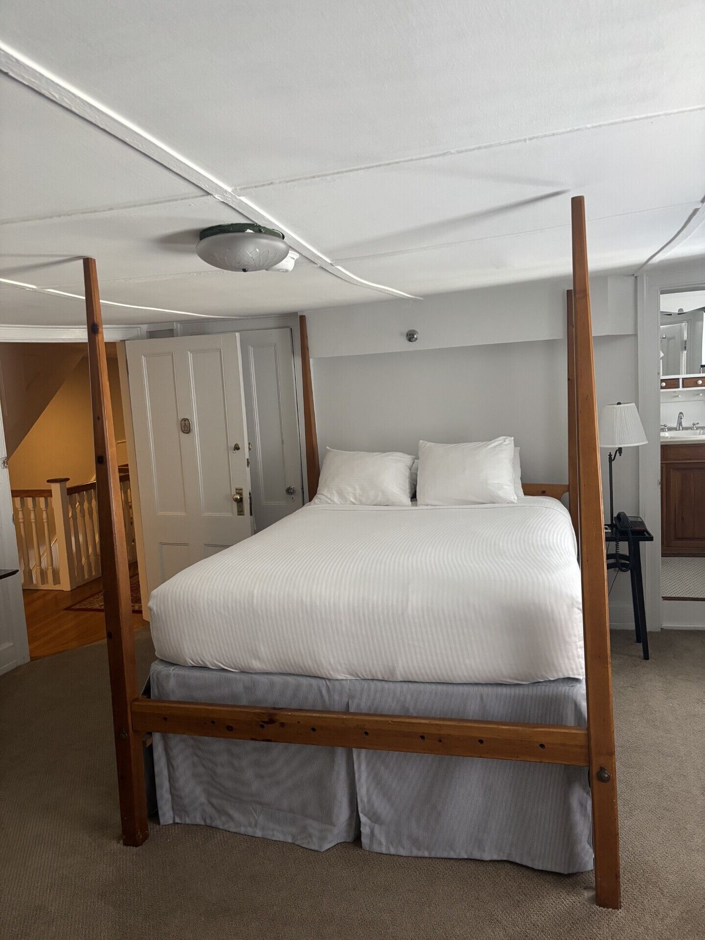 A four-poster bed in a hotel room with a wooden frame, white bedding, and a carpeted floor.