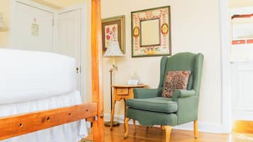Un dormitorio con una cama de madera, un sillón verde, una mesita con una lámpara y dos cuadros en la pared.