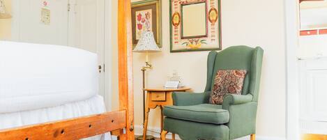 A bedroom with a wooden bed, a green armchair, a small table with a lamp, and two framed pictures on the wall.