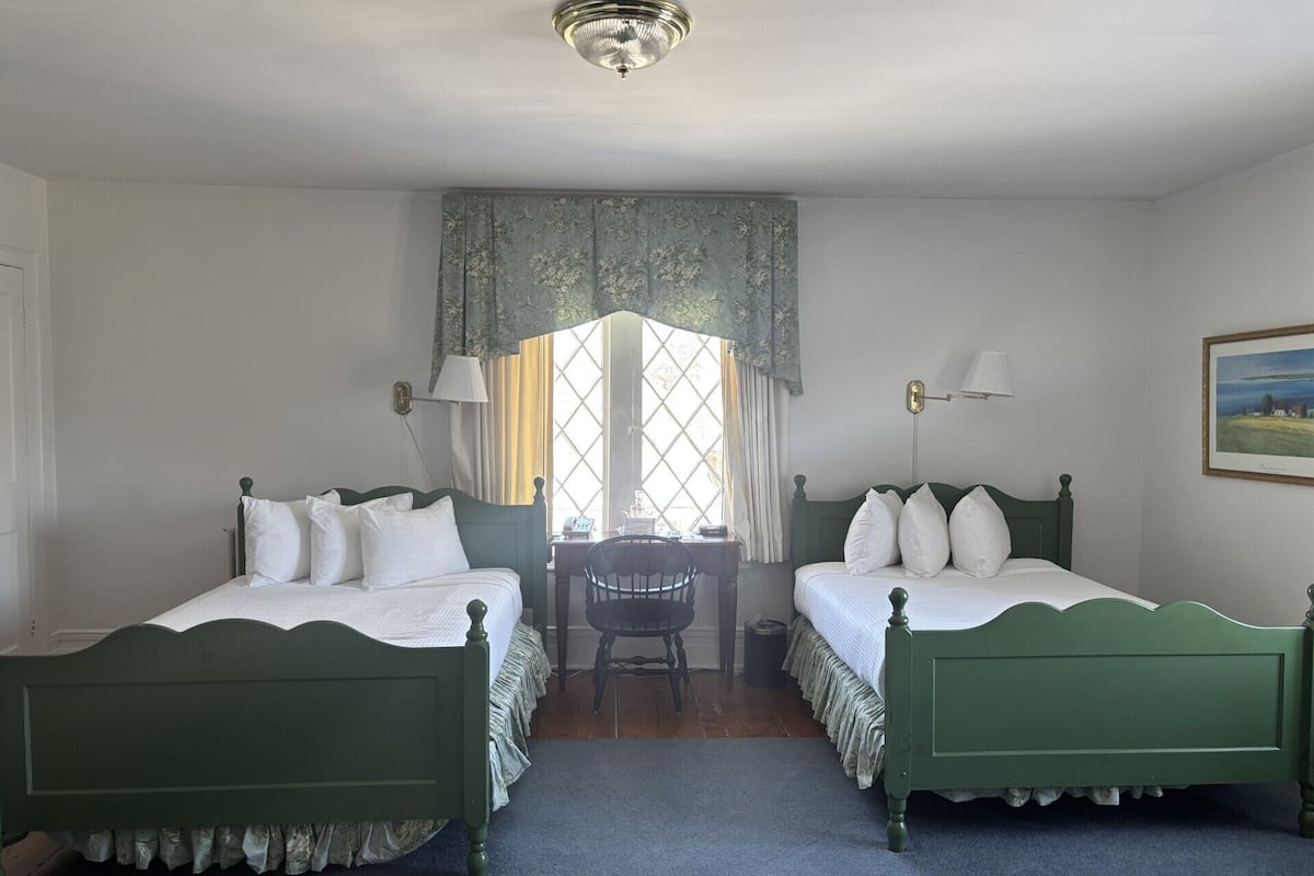 A room with two green beds, a small table, and a window with curtains.