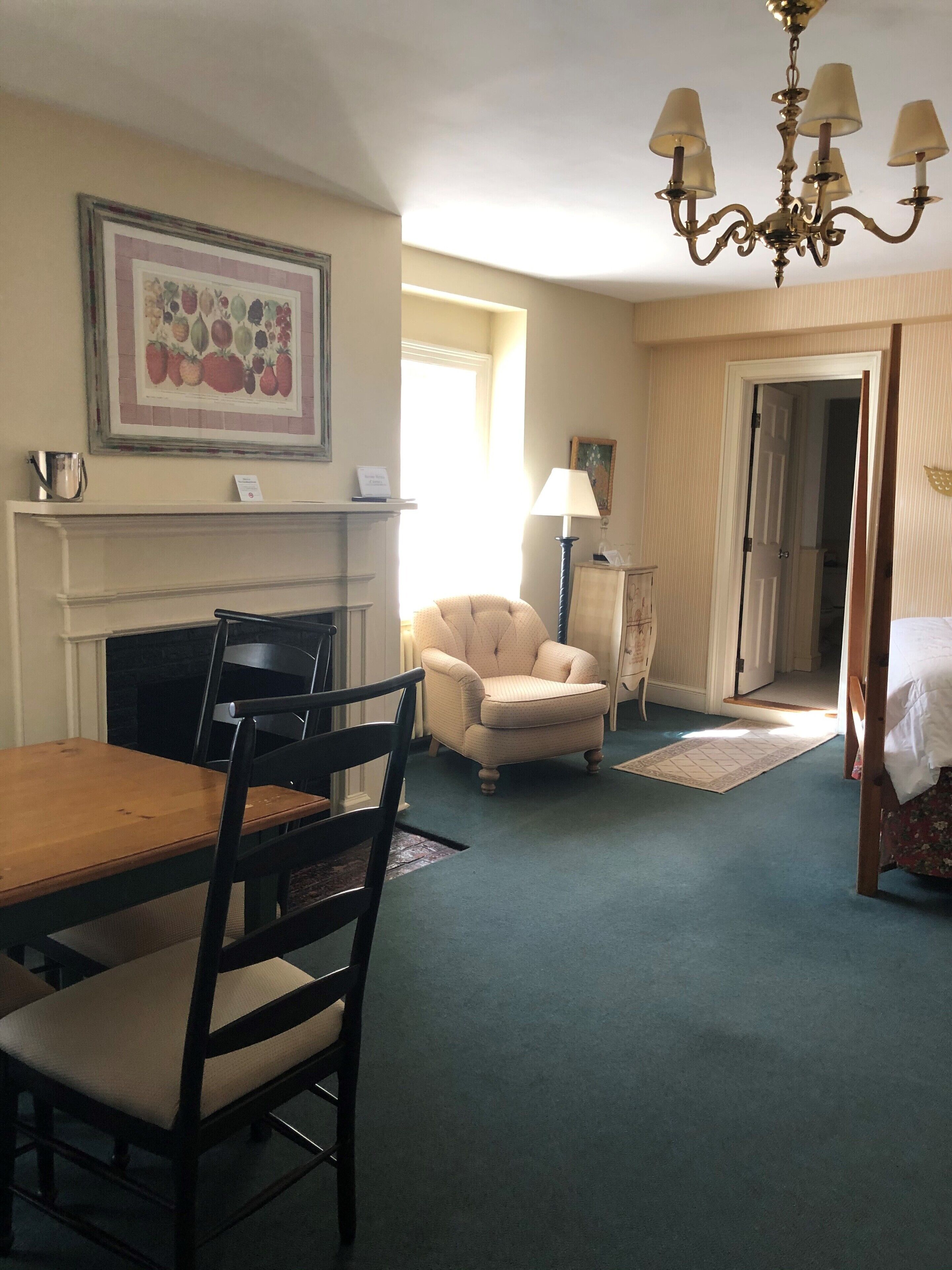 A room with a dining table, chairs, a fireplace, a chandelier, and a door leading to another room.