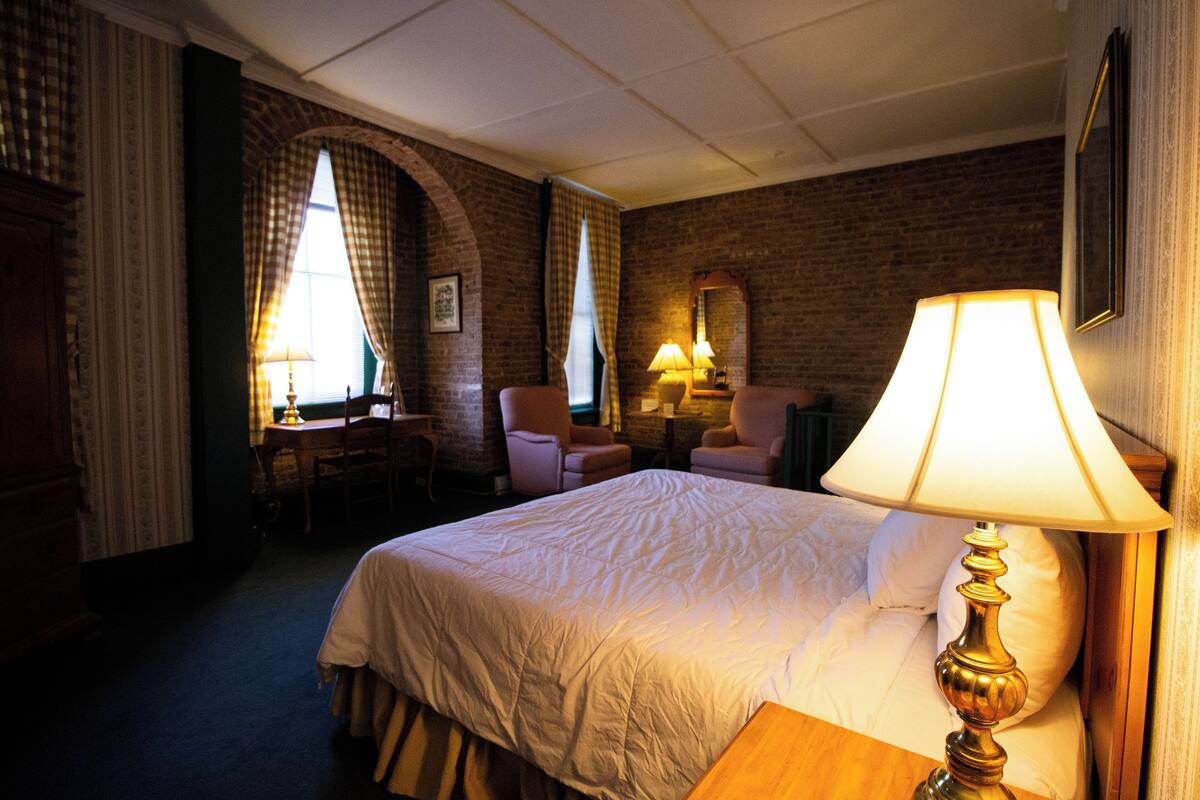 A hotel room with a large bed, two armchairs, a desk, and a lamp.