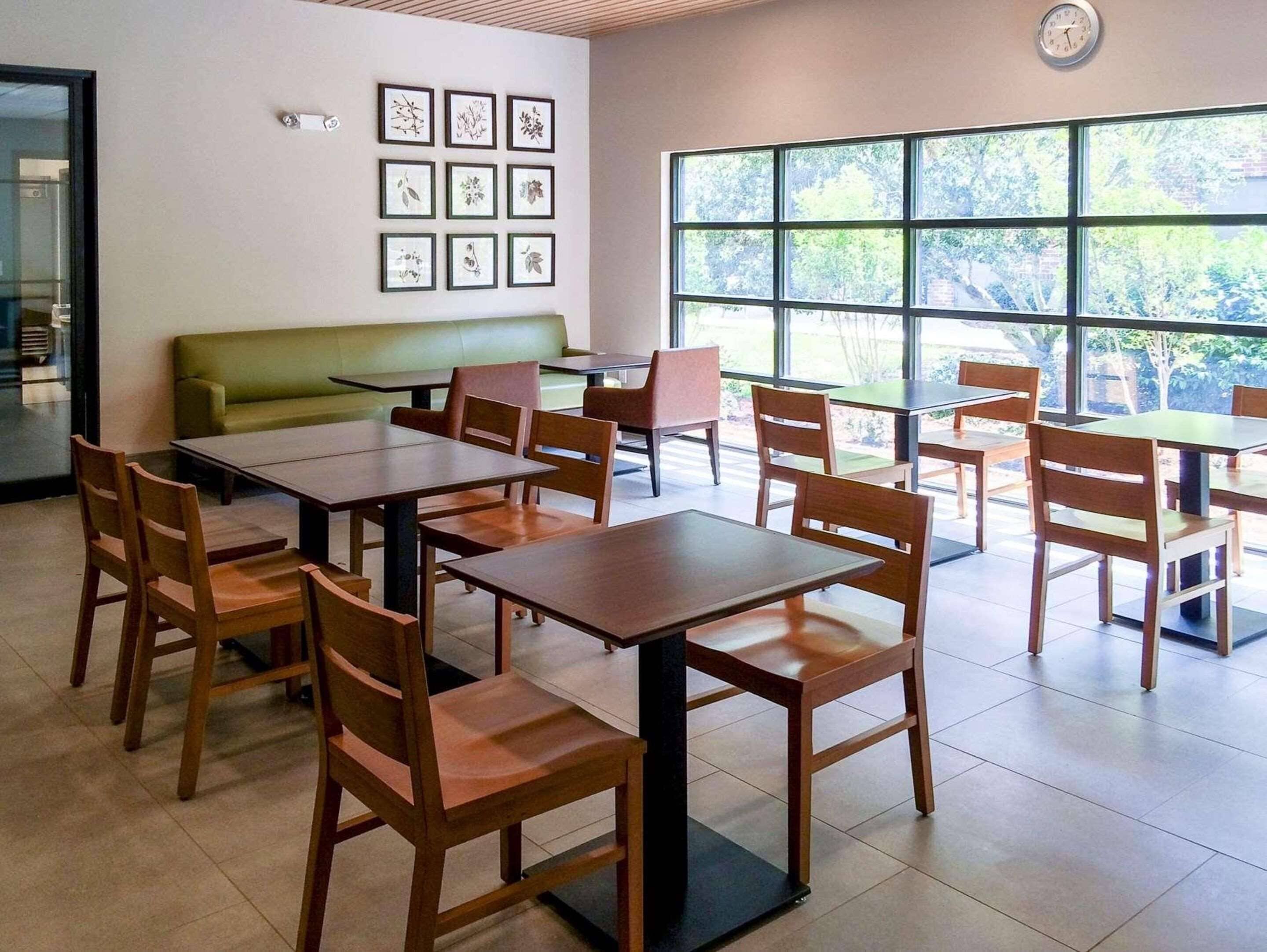 A dining area with tables and chairs, a green sofa, and framed botanical prints on the wall.