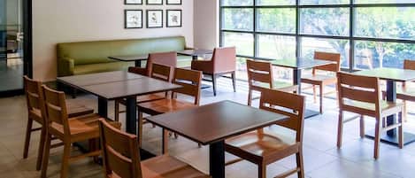 A dining area with tables and chairs, a green sofa, and framed botanical prints on the wall.