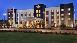 A modern hotel with a prominent entrance, multiple floors, and a flag. - Country Inn & Suites by Radisson, Smithfield-Selma, NC (Smithfield)