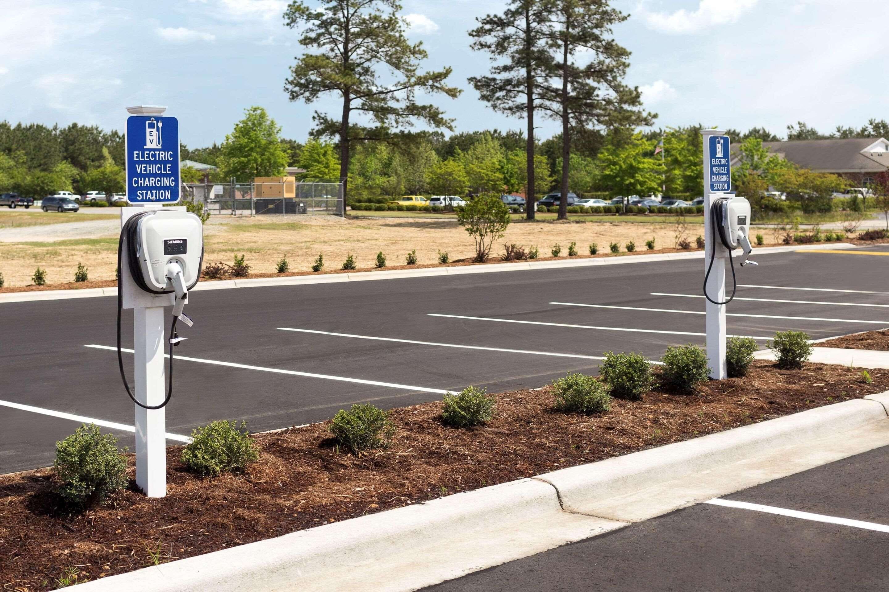 An electric vehicle charging station in a parking lot with trees and a building in the background.