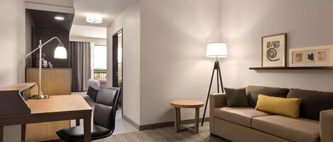 Habitación de hotel con escritorio, silla, sofá, lámpara y una obra de arte en la pared.