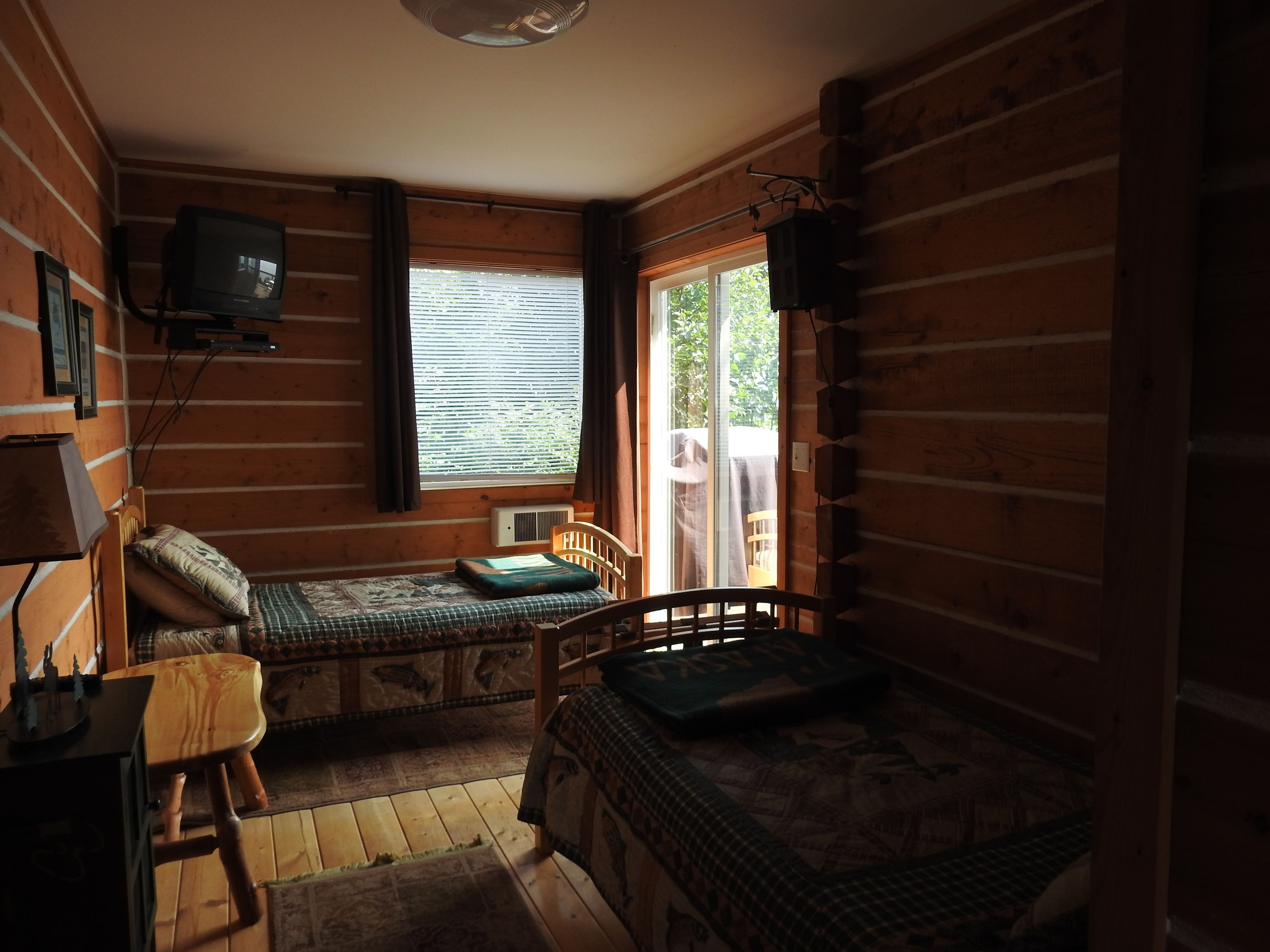 A cabin with two wooden beds, a small table, a television, and a window with blinds.