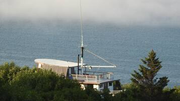 A coastal building with a large antenna, surrounded by dense greenery and overlooking the sea.