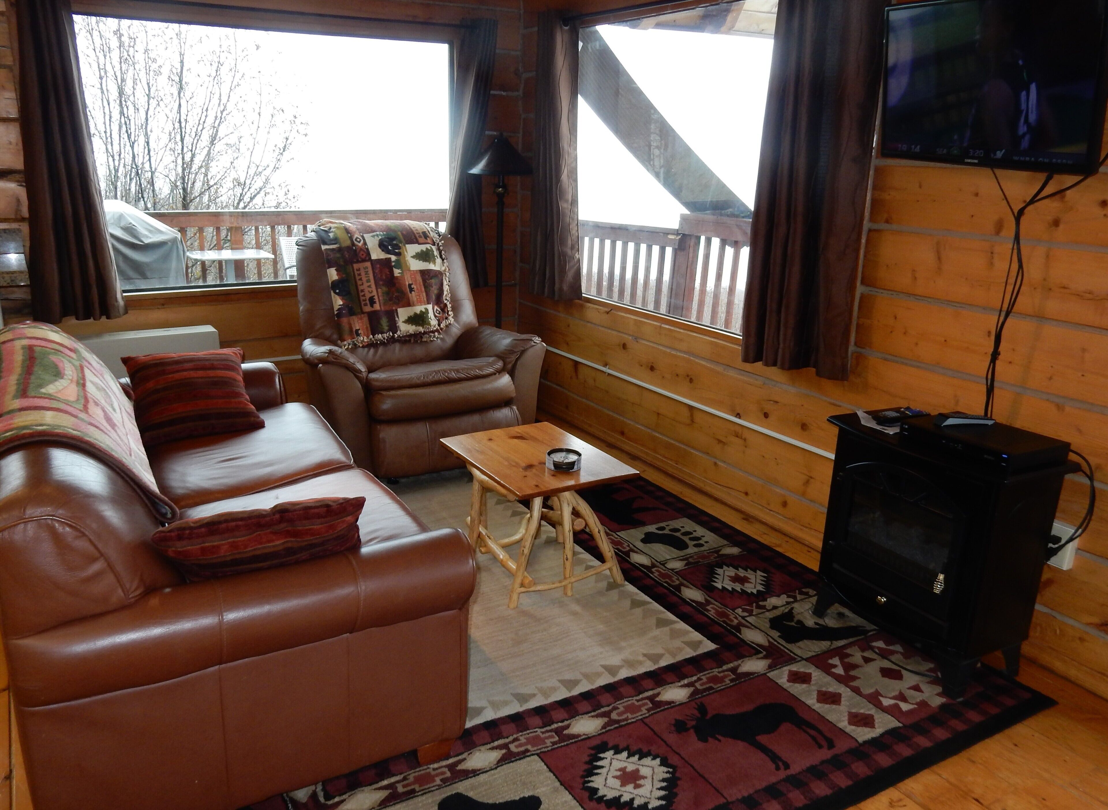 A cozy cabin interior with a leather sofa, a recliner, a small wooden table, a television, and a patterned rug.