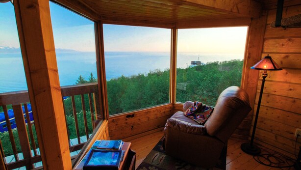 Une cabane en bois dotée d’une grande fenêtre donnant sur un lac et une forêt.