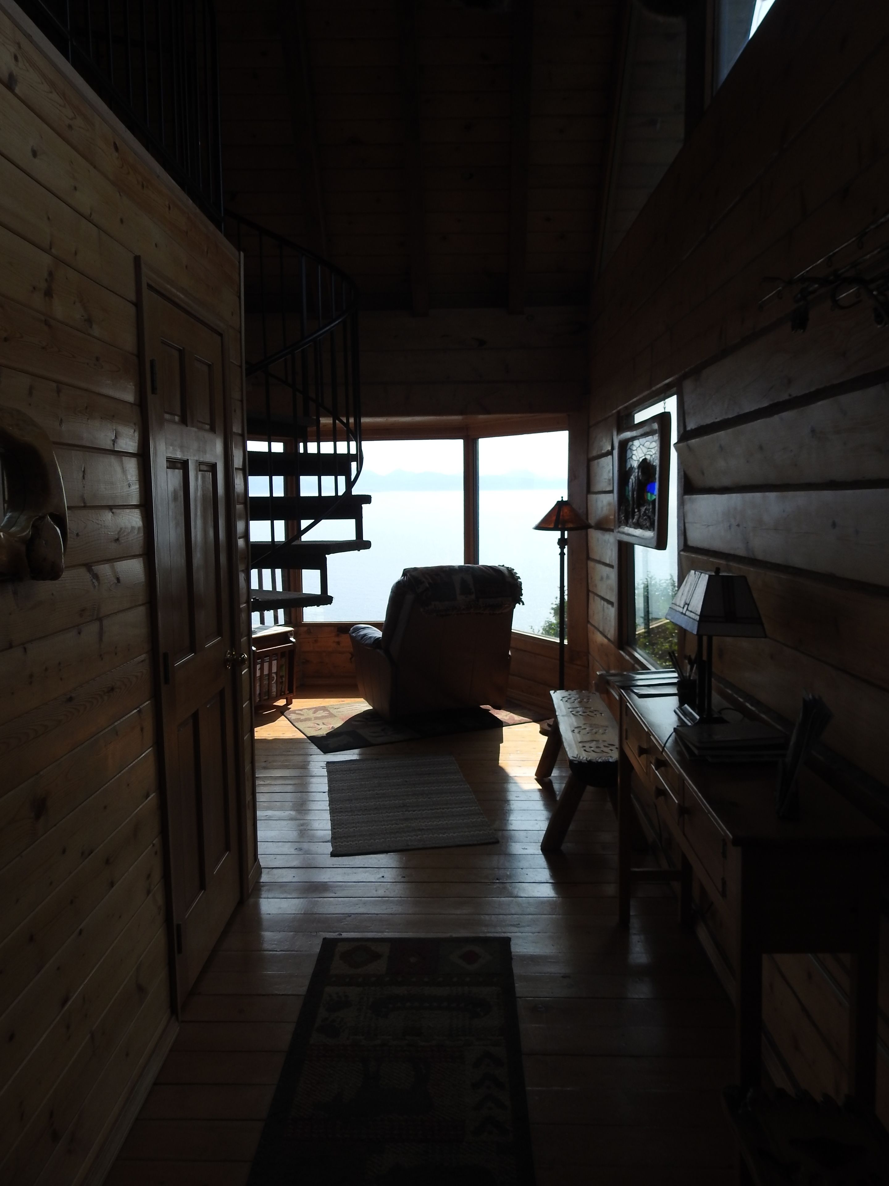 L’intérieur d’un chalet en bois, avec un escalier menant à un balcon, un canapé et un bureau avec une lampe.
