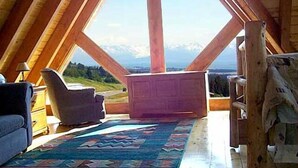 Une pièce aux hauts plafonds, avec un décor intérieur en bois, une grande fenêtre et une vue sur un paysage montagneux.