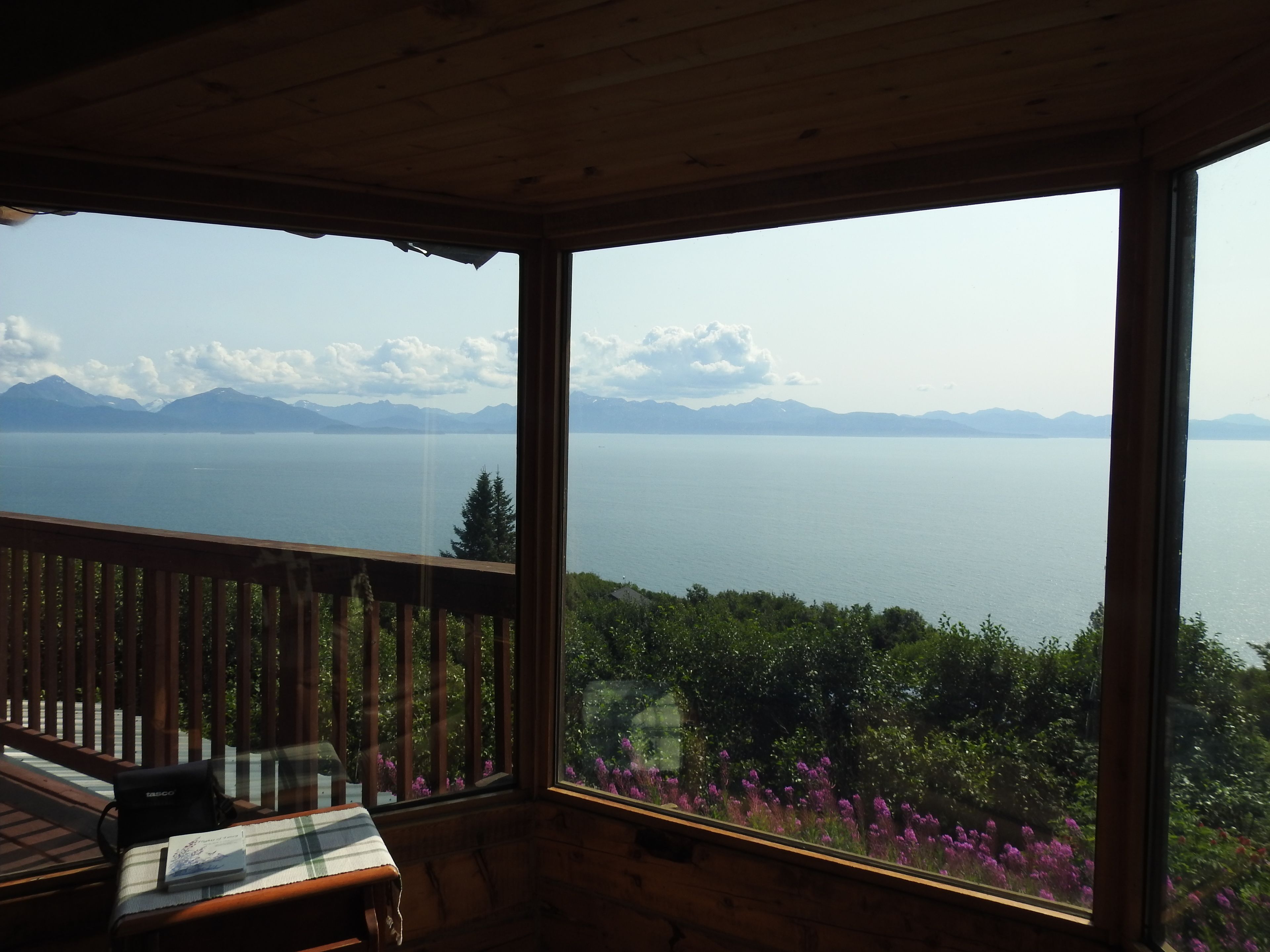 A wooden deck with a table and chairs, overlooking a lake with mountains in the distance.
