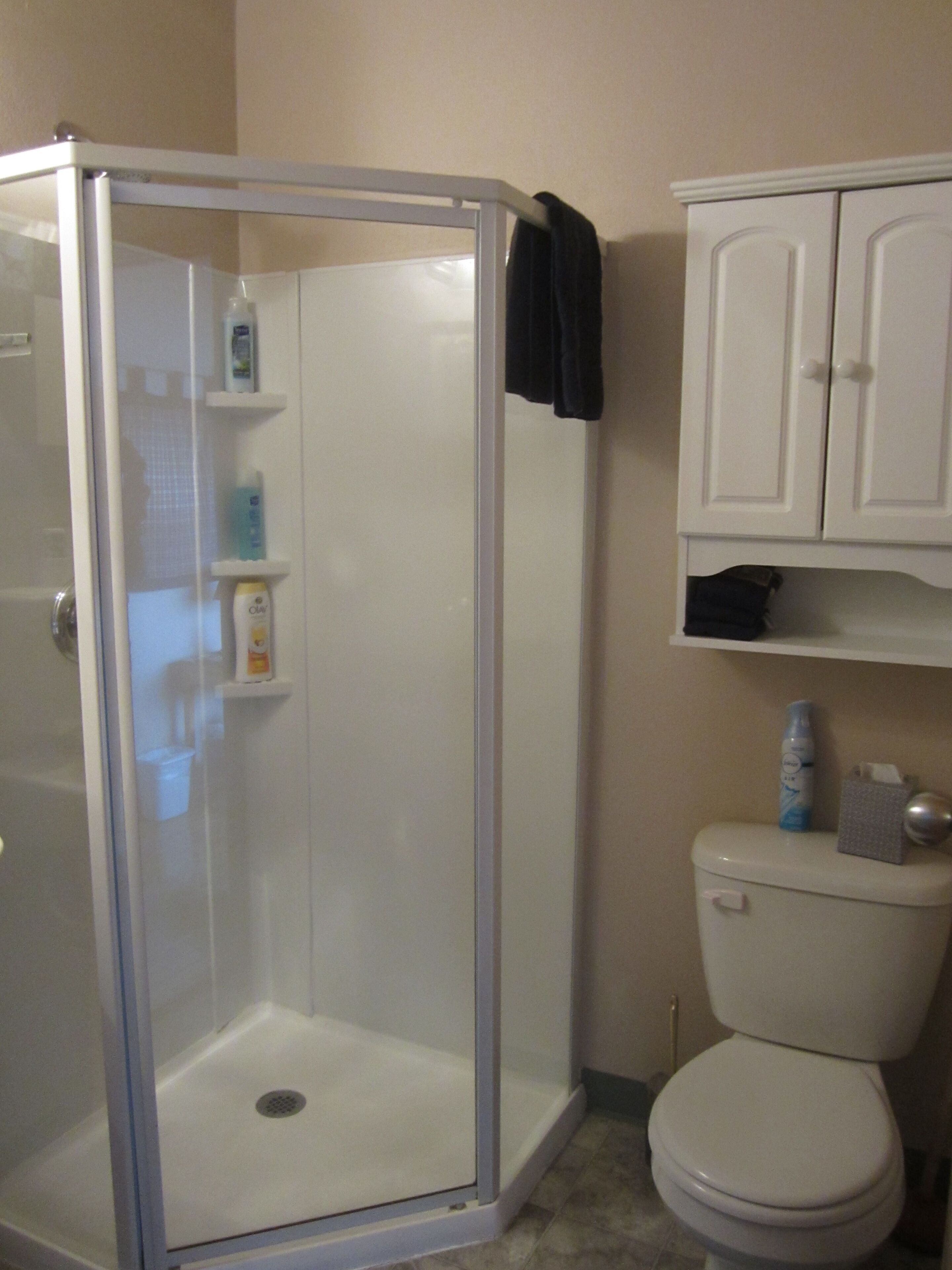 A bathroom with a glass-enclosed shower, a toilet, and a cabinet above the toilet.