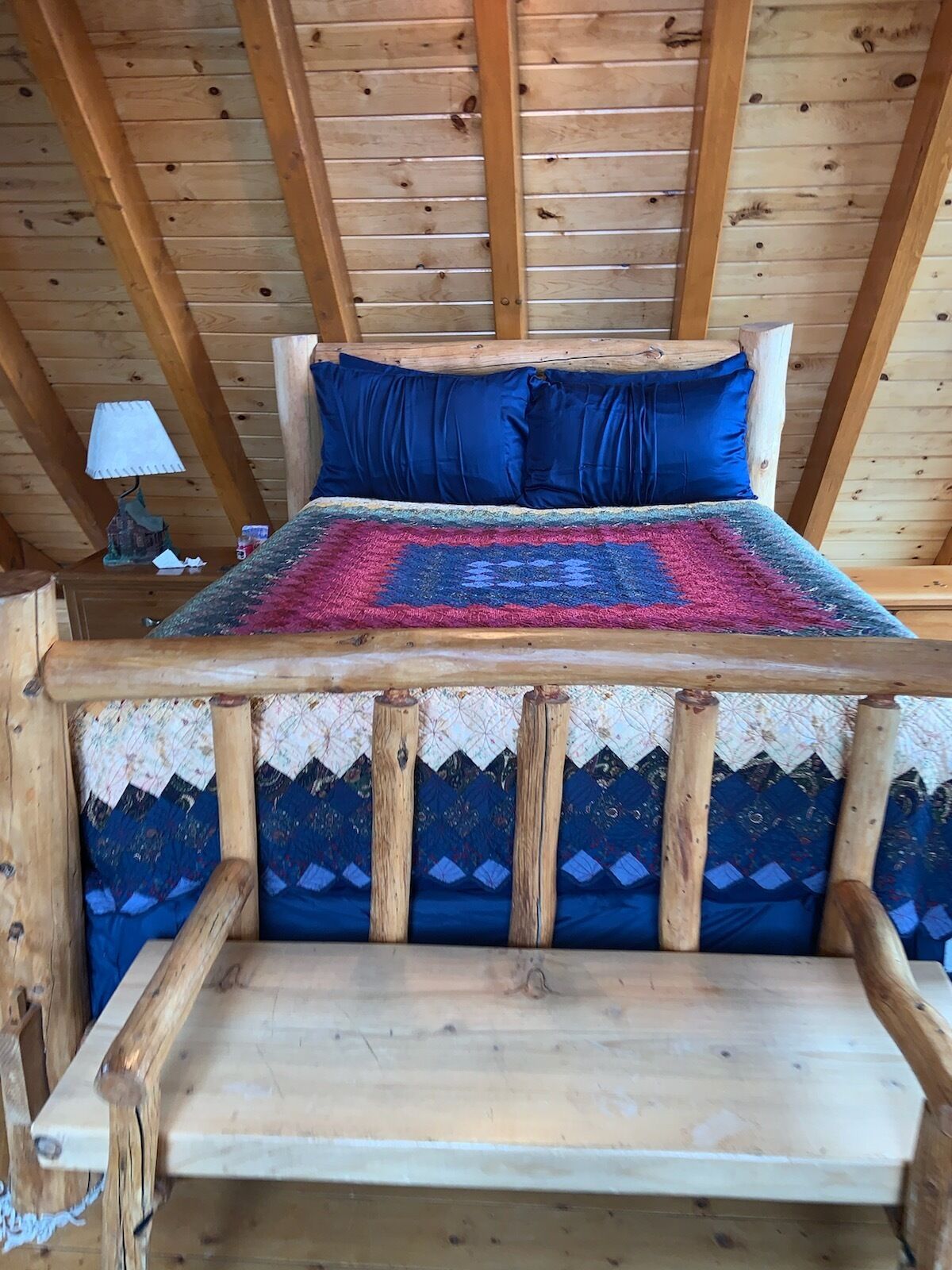 A wooden bed with a colorful blanket and pillows, set in a room with a wooden ceiling and walls.