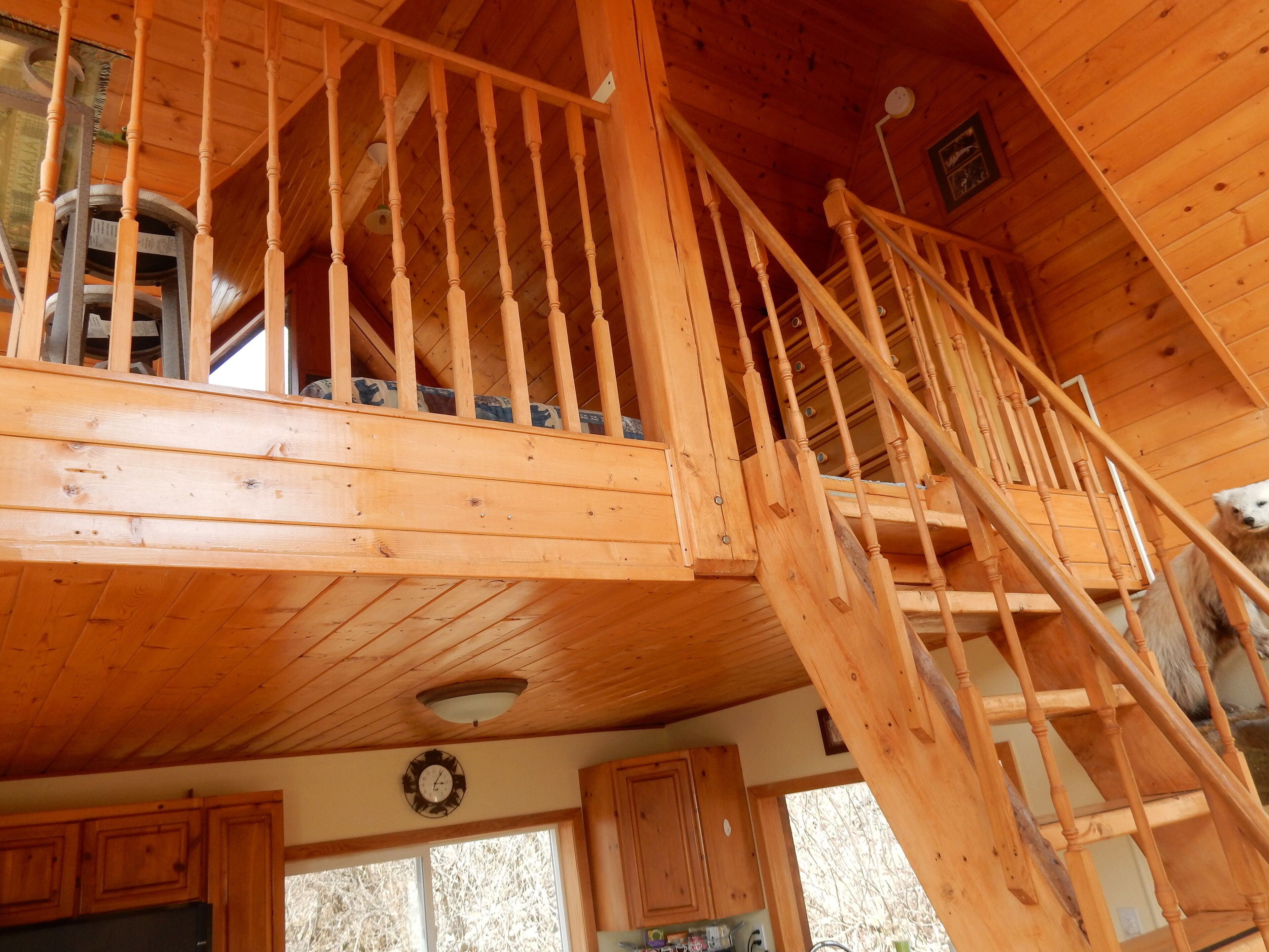 L’intérieur d’une cabane en bois, avec un escalier reliant les deux étages, un coin cuisine et une fenêtre donnant sur l’extérieur.