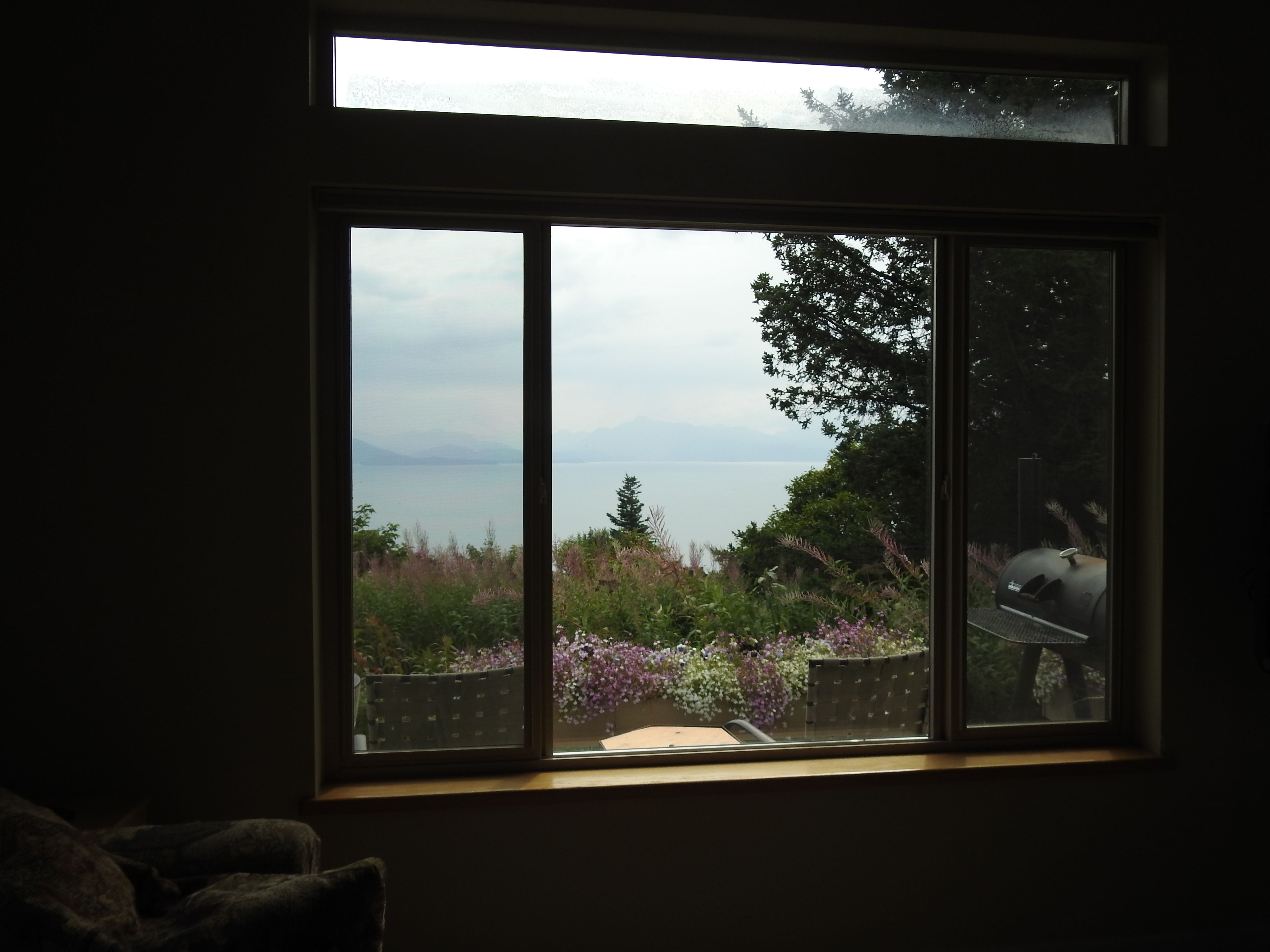 A room with a large window overlooking a garden and a body of water.