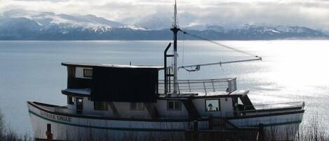 A boat with a cabin and a small deck area, docked near a body of water with mountains in the background.