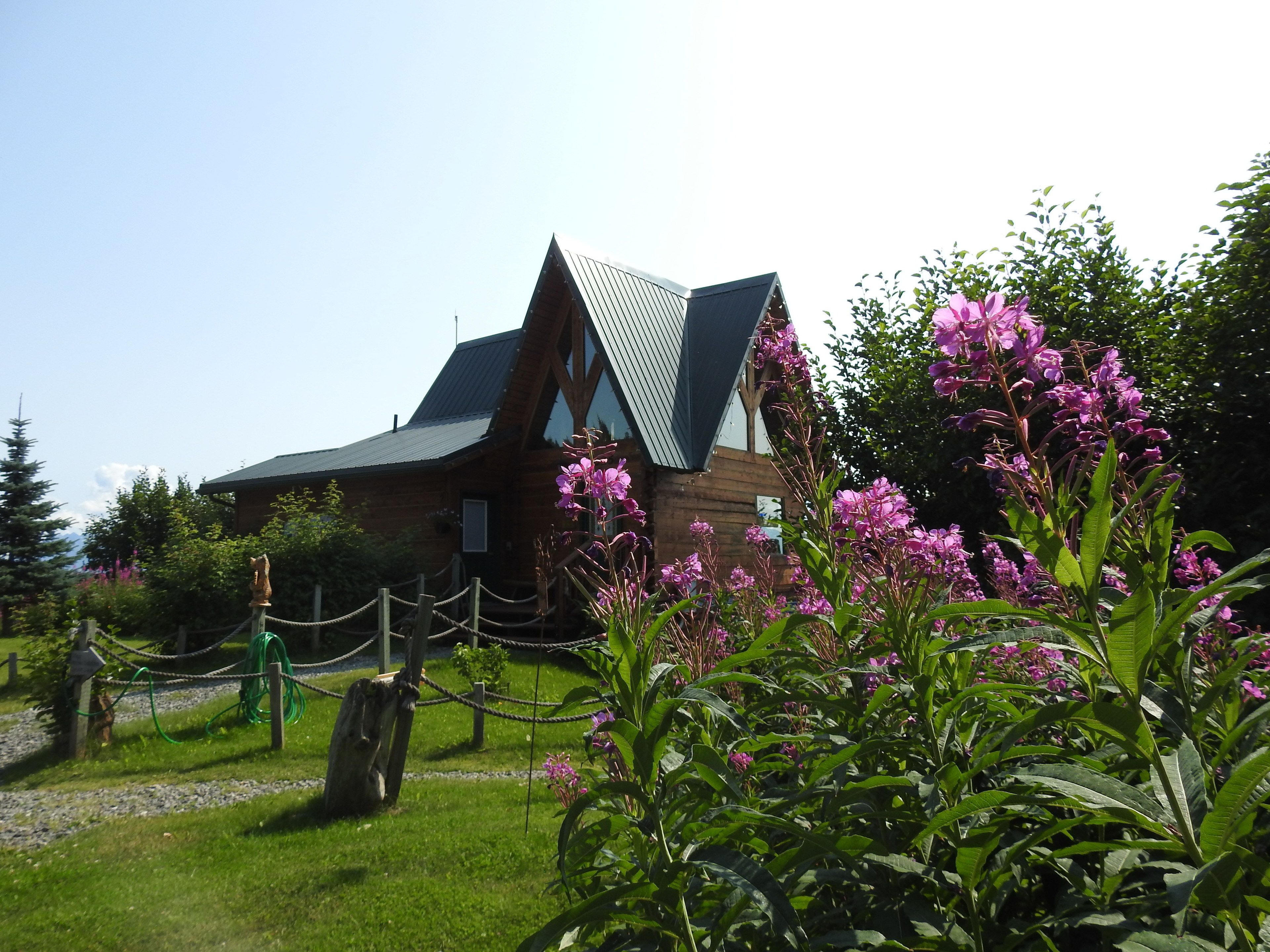 Une cabane en bois avec un toit en pente et un jardin clos agrémenté de fleurs roses.