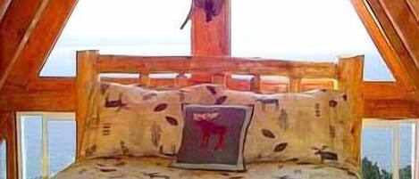 Une chambre à coucher aménagée dans les combles, avec un plafond en pente, un lit doté de linge de lit aux motifs animaliers et une fenêtre donnant sur un paysage.