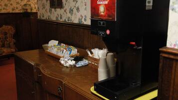 Una máquina de café con etiqueta Douwe Egberts, una cesta de aperitivos y vasos de papel apilados sobre una encimera de madera.